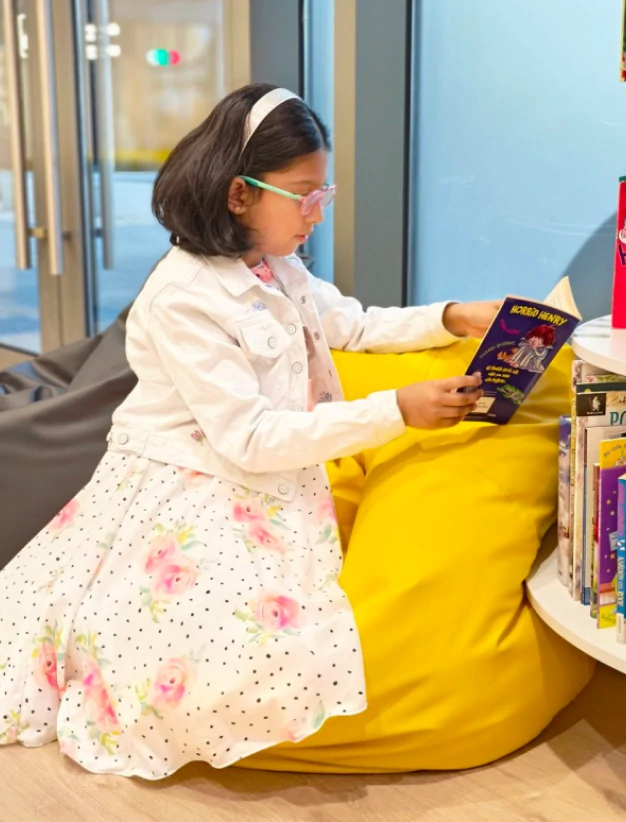 A girl reading in the waiting area of Oohlala Fine Arts while waiting for her music classes.