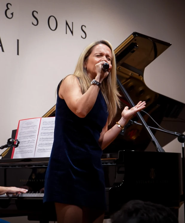 A singer performing during a presentation, accompanied by an Oohlala Fine Arts teacher on the piano.